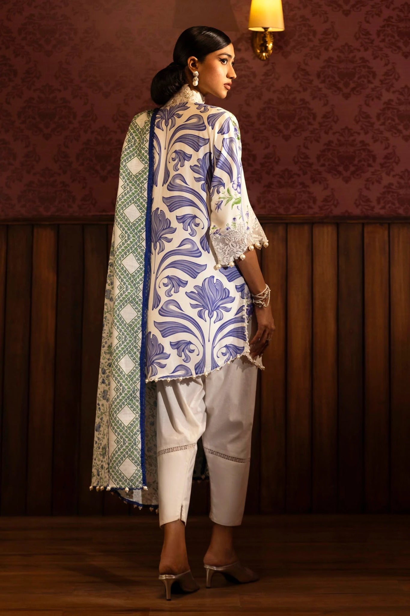 Model wearing a floral 3 - piece suit from Sana Safinaz Muzlin Winter 2024 collection, featuring digital printed linen front, back, and sleeves with embroidered neckline and sleeves, paired with a khaddar dupatta and dyed cotton pants.