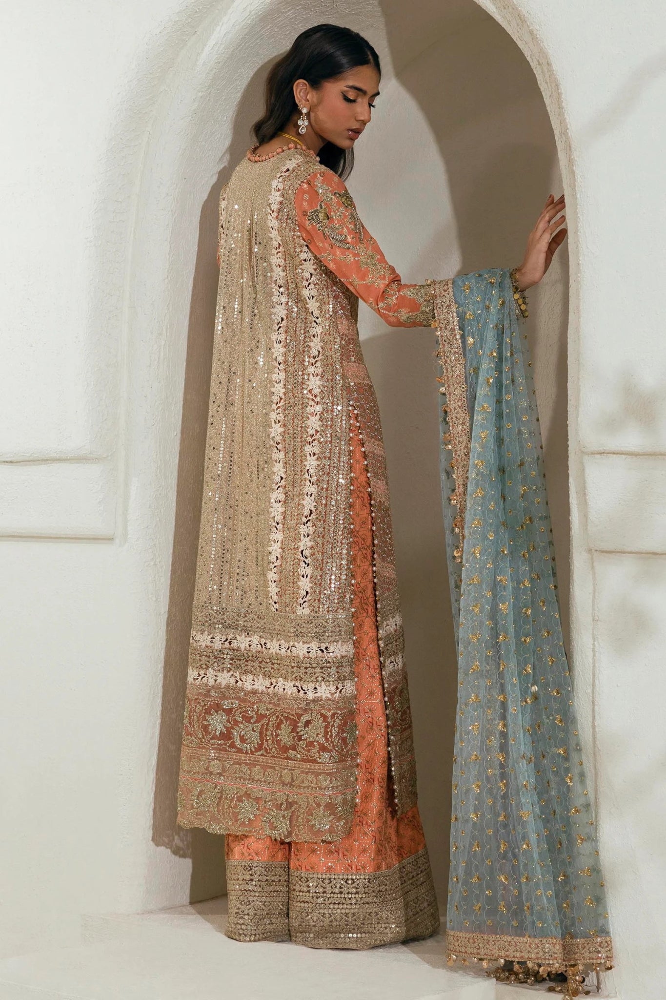 Model wearing a gold and orange Sana Safinaz NURA Festive'24 Vol. II N242 - 002 - 3CX dress with intricate embroidery and a blue dupatta. Perfect for weddings and available online in the UK.