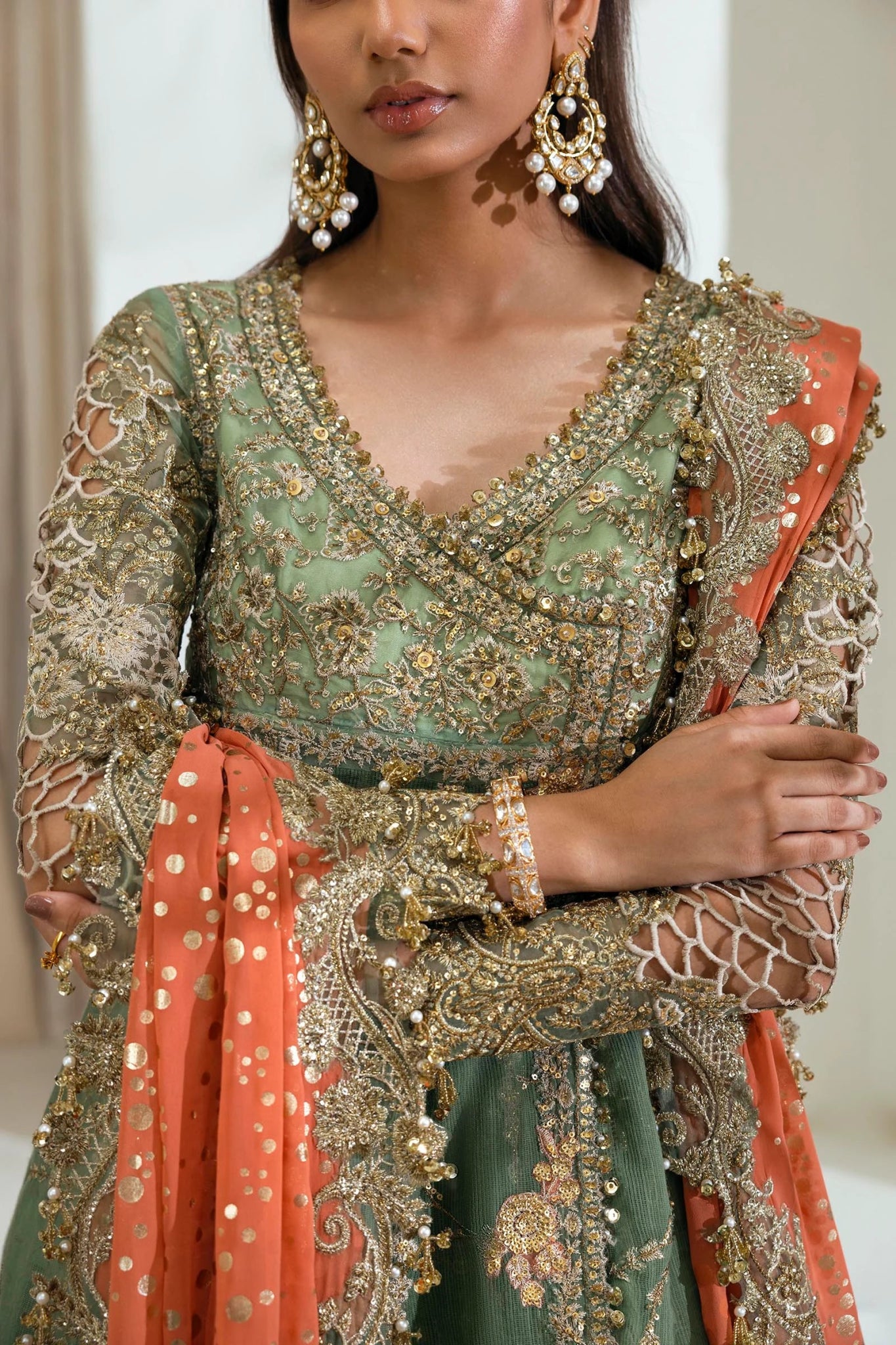 Model wearing Sana Safinaz NURA Festive'24 Vol. II N242 - 006 - 3CX dress, featuring a green ensemble with gold embellishments and an orange dupatta. Perfect for weddings and available as Pakistani clothes online in the UK.