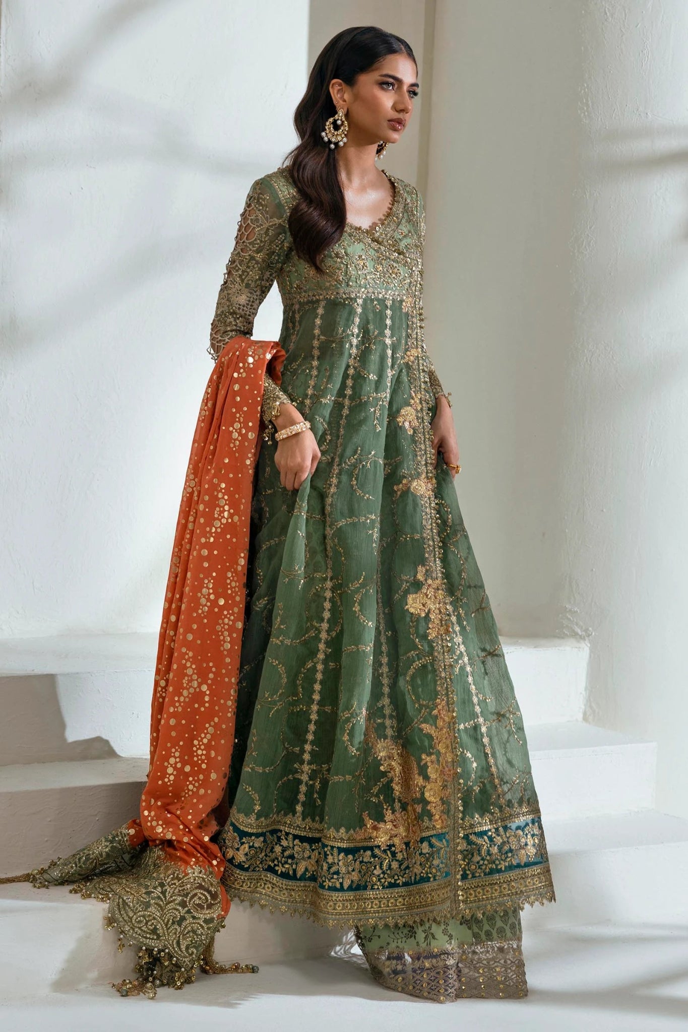 Model wearing Sana Safinaz NURA Festive'24 Vol. II N242 - 006 - 3CX dress, featuring a green ensemble with gold embellishments and an orange dupatta. Perfect for weddings and available as Pakistani clothes online in the UK.