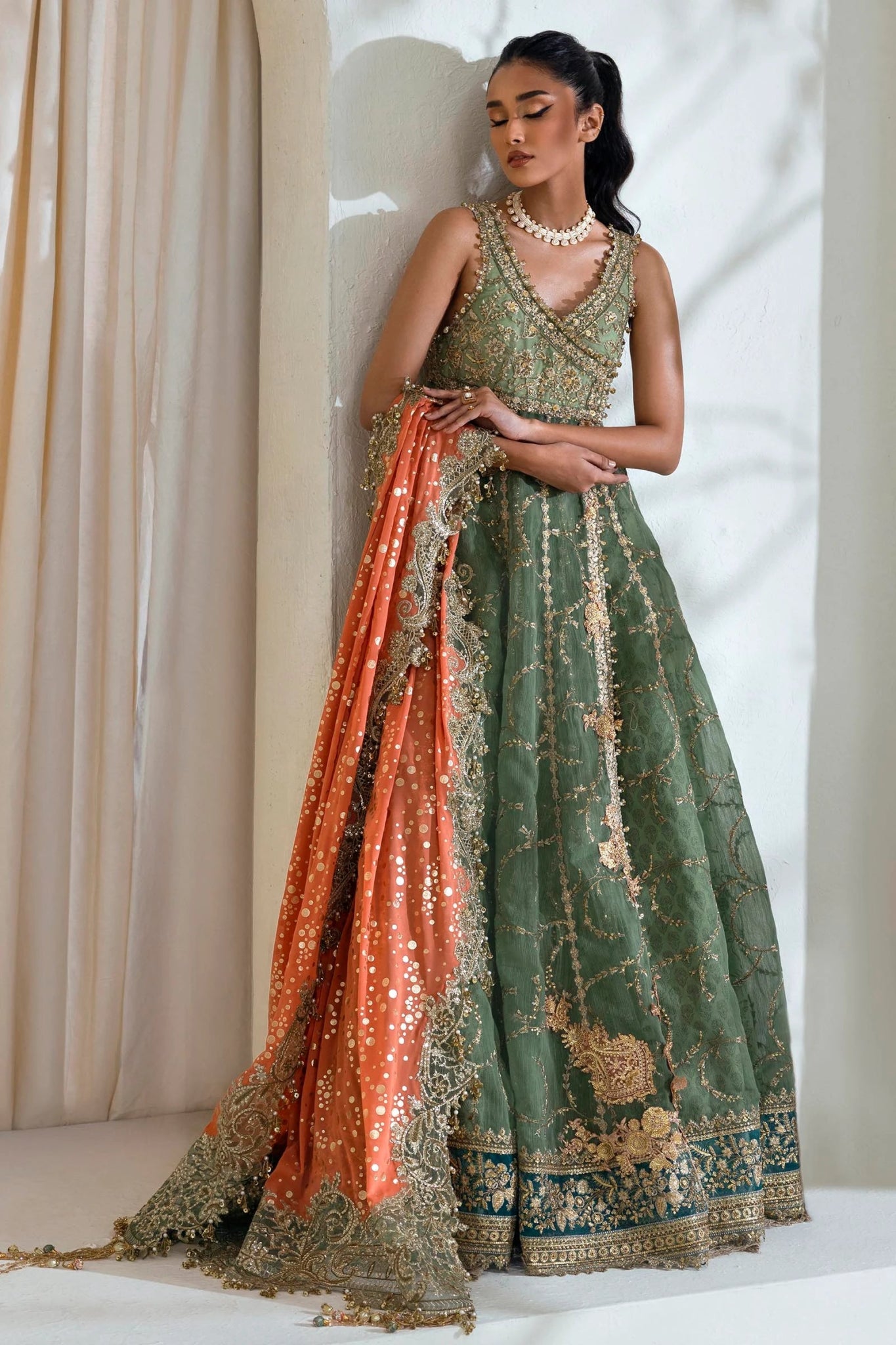 Model wearing Sana Safinaz NURA Festive'24 Vol. II N242 - 006 - 3CX dress, featuring a green ensemble with gold embellishments and an orange dupatta. Perfect for weddings and available as Pakistani clothes online in the UK.