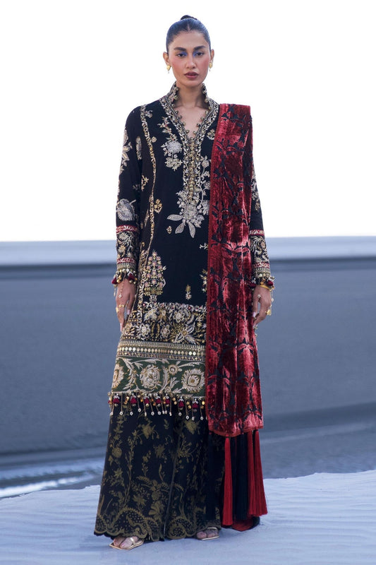 Model wearing Sana Safinaz Winter Luxury '24 S241 - 001A - 3CP, a black and gold embroidered outfit with intricate patterns and a bold red velvet shawl. Perfect for winter, available for Pakistani clothes online in the UK.