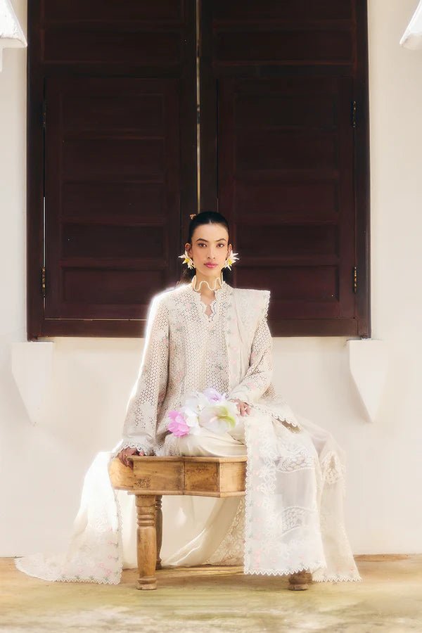 Model wearing a Suffuse Fall Casual Pret'24 which is an ivory lawn shirt with floral patchwork in soft pinks and pastel greens, paired with wide - leg cotton pants and a chiffon dupatta adorned with organza floral details and lace accents. Available online in UK.