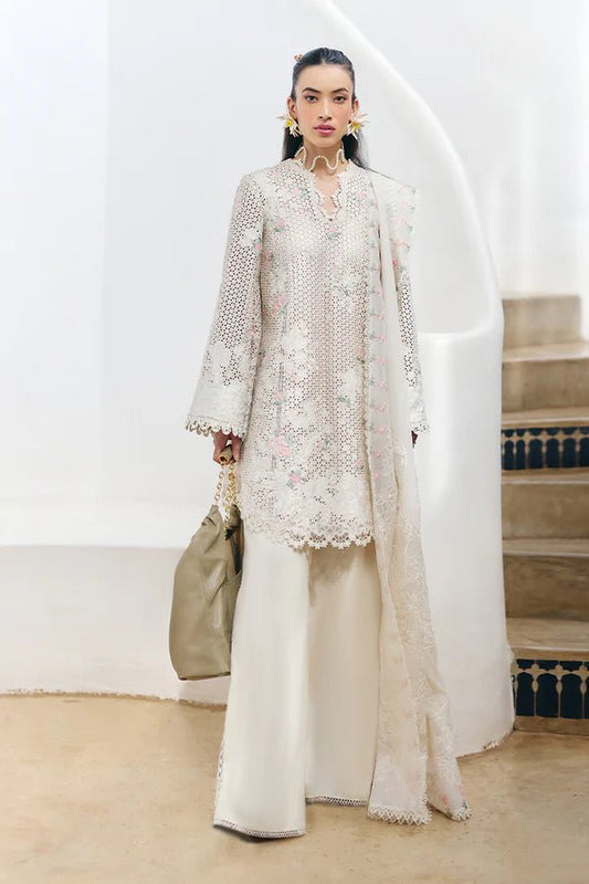 Model wearing a Suffuse Fall Casual Pret'24 which is an ivory lawn shirt with floral patchwork in soft pinks and pastel greens, paired with wide - leg cotton pants and a chiffon dupatta adorned with organza floral details and lace accents. Available online in UK.