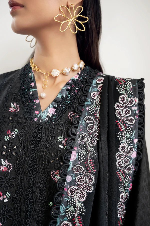 Model wearing a black jacquard front open A - line kurta with pastel floral embroidery, wide sleeves, and a printed raw silk neckline. Paired with black straight pants featuring lace detailing and a chiffon dupatta with embroidered borders and geometric patterns. This look is from Suffuse's Fall Casual Pret 24 Collection.