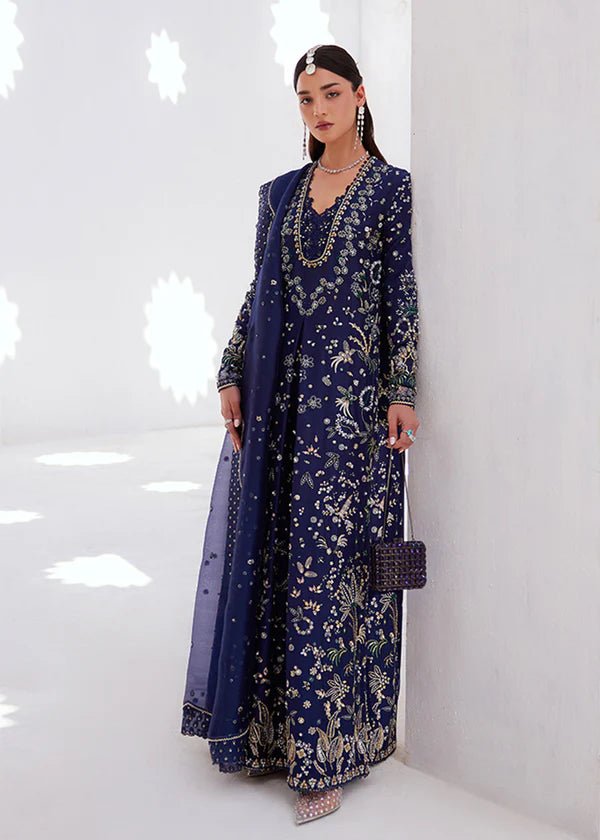 Model wearing a deep blue dress with intricate gold and green embroidery from the Suffuse FREESHIA RTW '24 Aroosh collection. Perfect for weddings. Pakistani clothes online in UK.