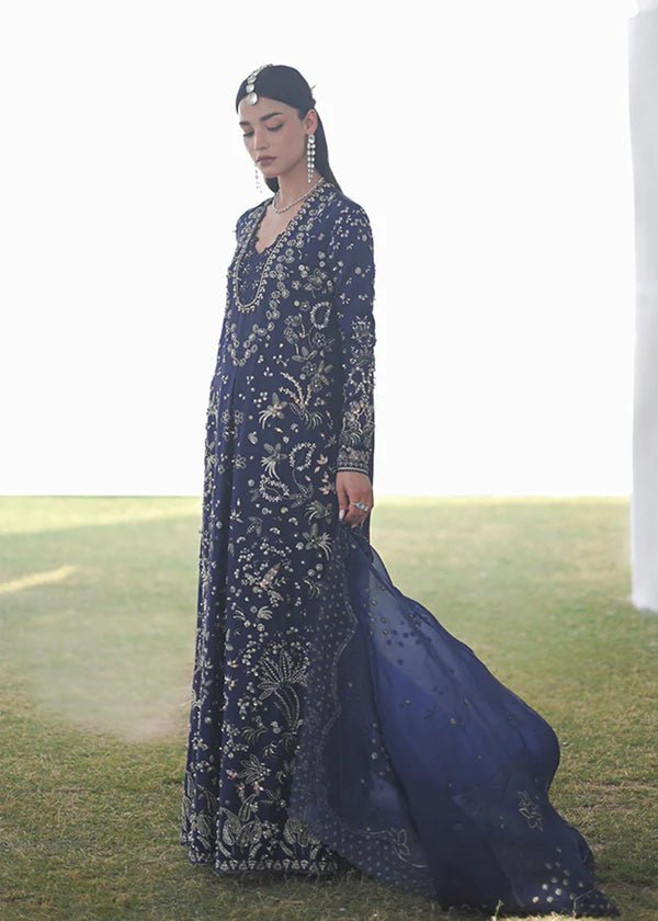 Model wearing a deep blue dress with intricate gold and green embroidery from the Suffuse FREESHIA RTW '24 Aroosh collection. Perfect for weddings. Pakistani clothes online in UK.